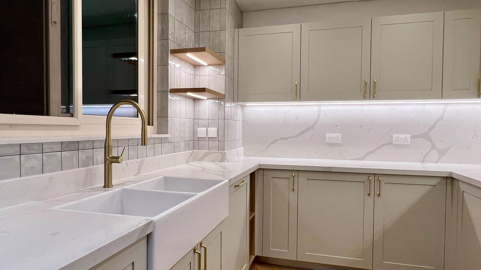 Kitchen renovation in Dubai showcasing quartz countertops, farmhouse sink, matte cabinetry, and under-cabinet lighting.